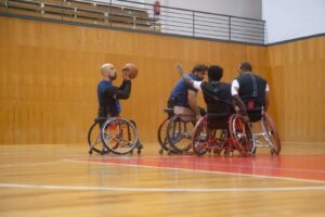 A group of athletes playing wheelchair basketball indoors on a wooden court.
