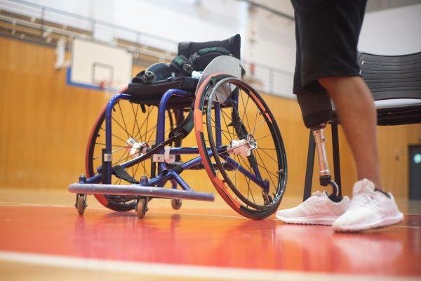 Close-up of a wheelchair and prosthetic leg on a basketball court emphasizing adaptive sports.